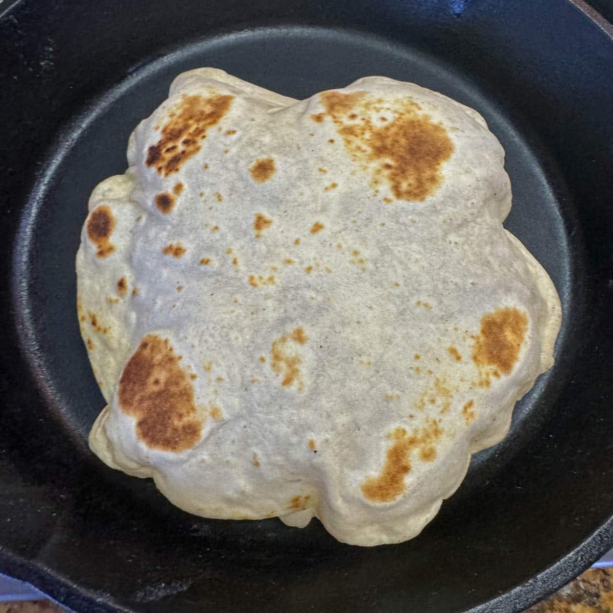 puffed up sourdough discard flour tortilla in a cast iron pan.