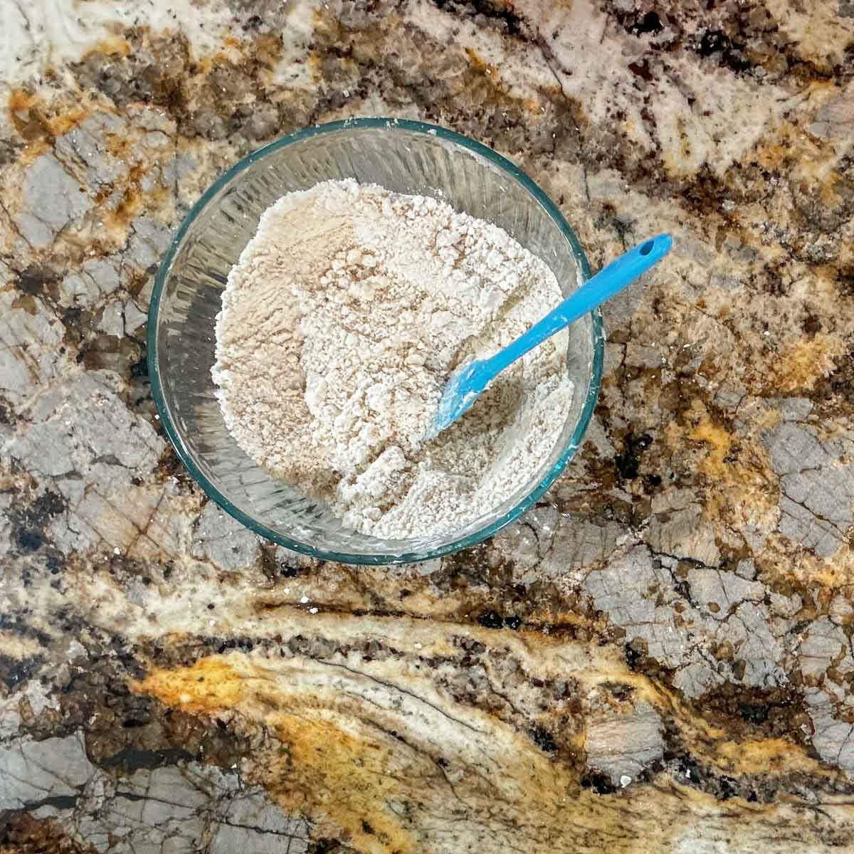 flour mixture in a glass bowl with a blue spatula.