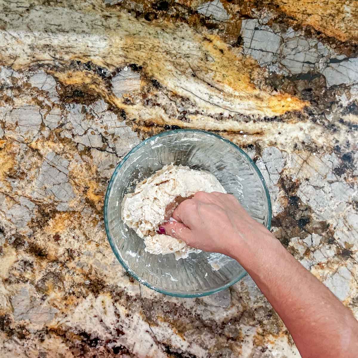 kneading tortilla dough in a glass bowl.