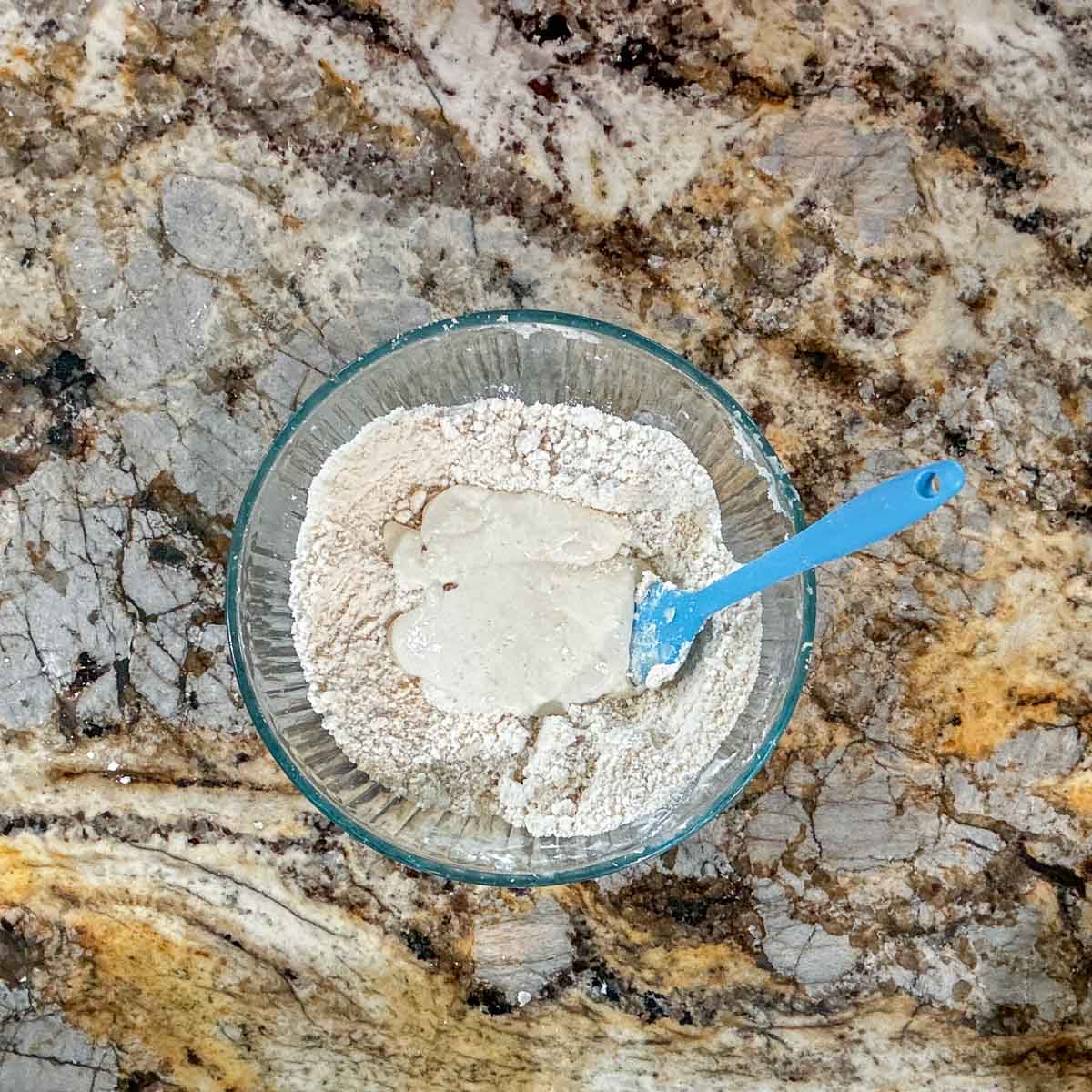 flour mixture and sourdough discard in a glass bowl with a blue spatula.