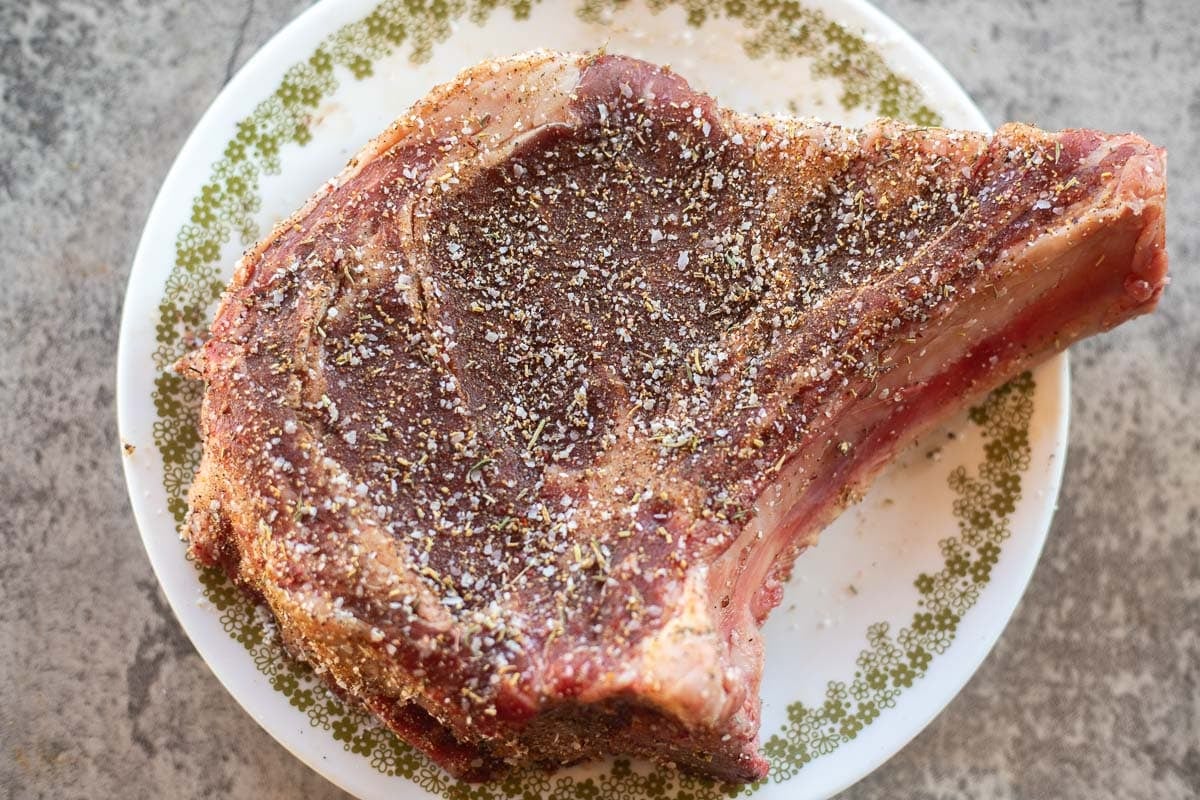 a raw seasoned steak on a white plate with green trim.