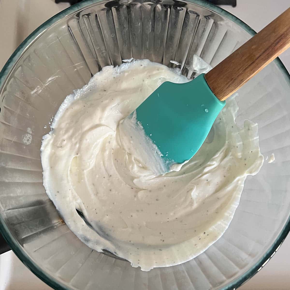 yogurt being warmed on double boiler with blue rubber spatular mixing it.