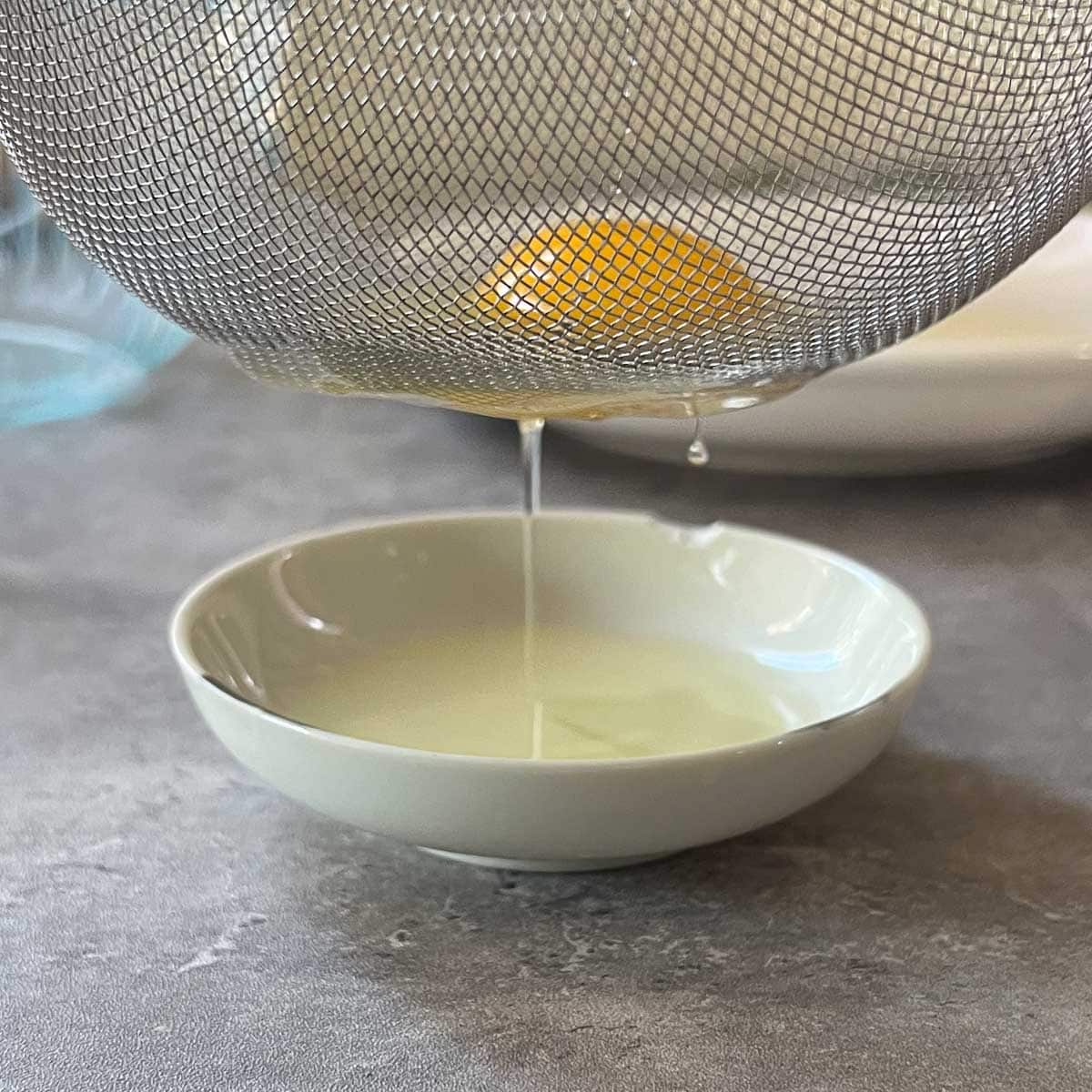 outer albumen draining through bottom of fine mesh strainer into small dish.