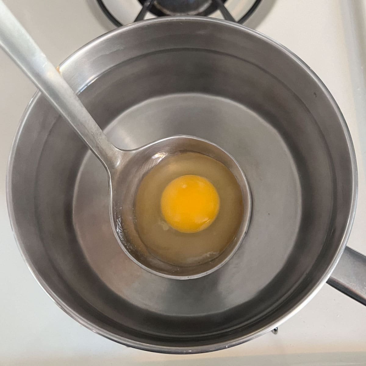 raw egg being lowered into water in a ladle.