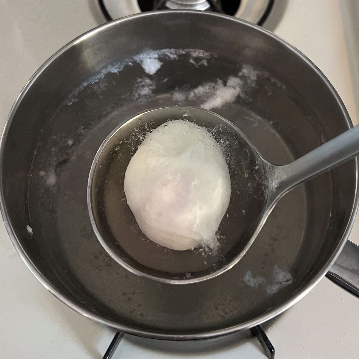 poached egg being removed from water with ladle.