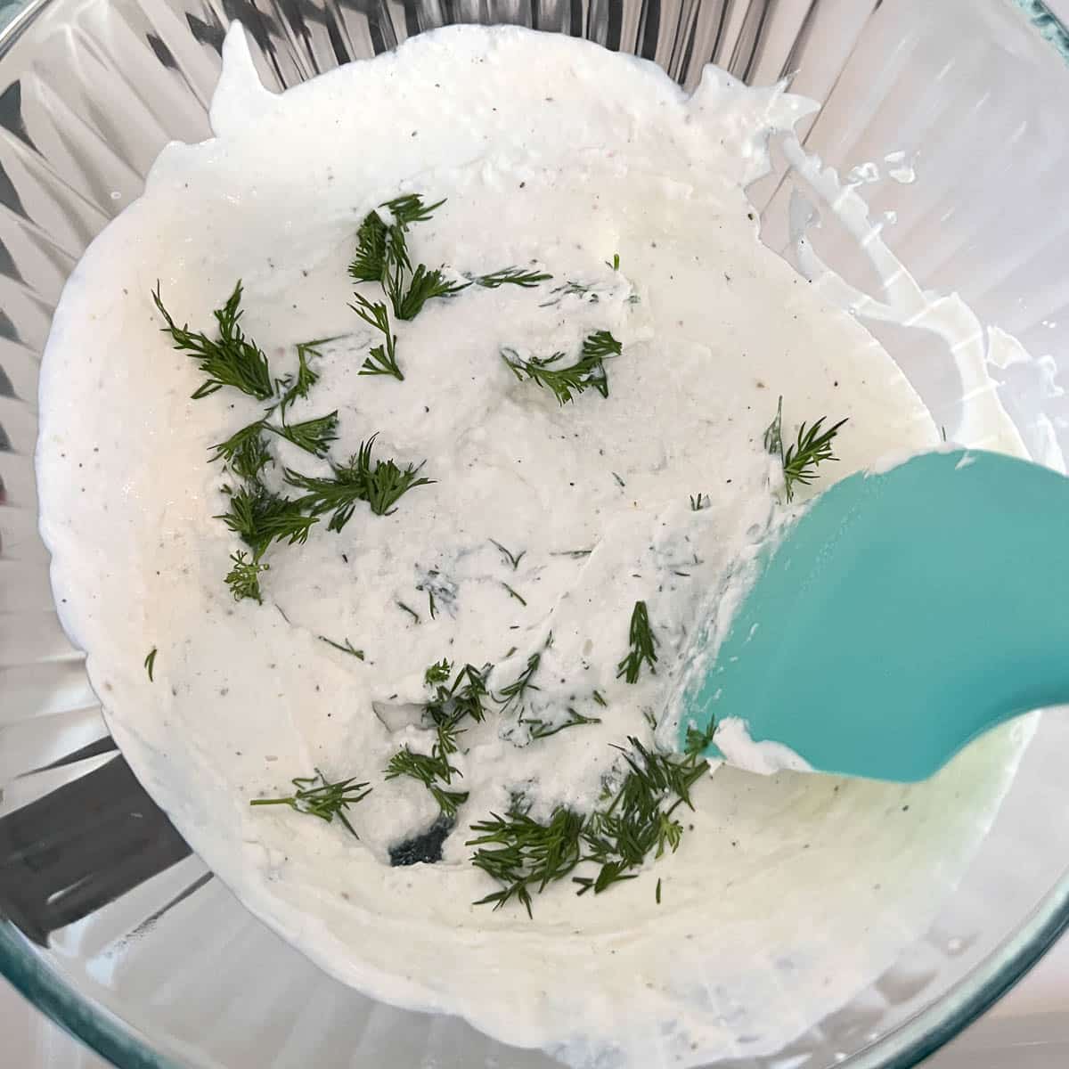 mixing fresh dill into yogurt with a blue spatula.