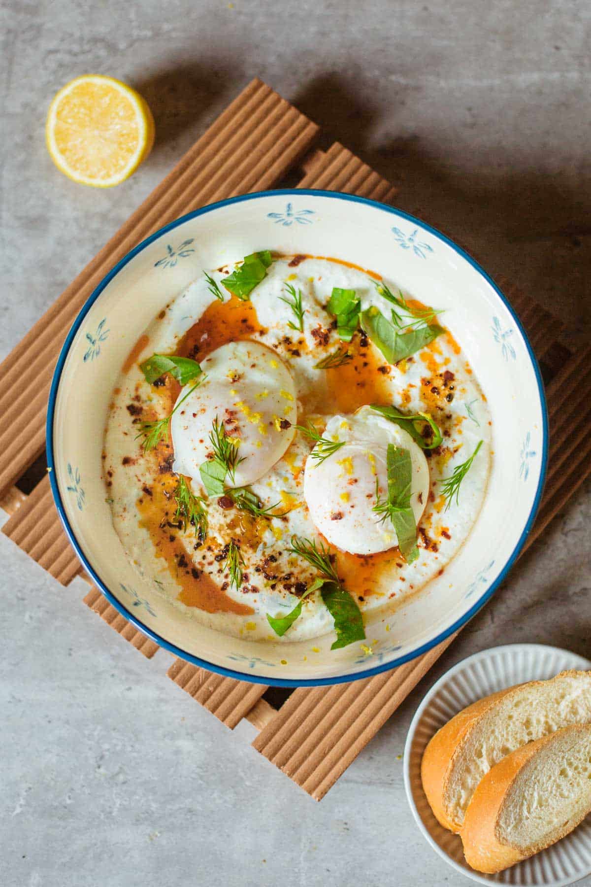 turkish eggs recipe (cilbir) in a bowl with fresh herbs, sliced baguette, and spoon.