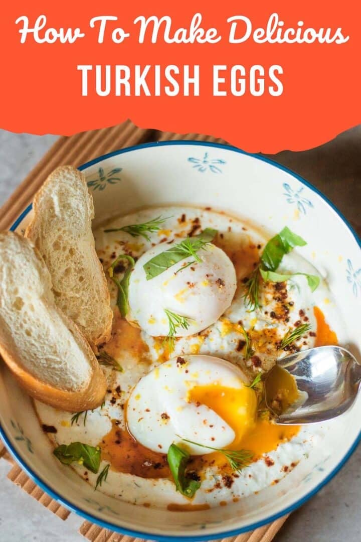 turkish eggs (cilbir) in a bowl with fresh herbs, sliced baguette, and spoon.