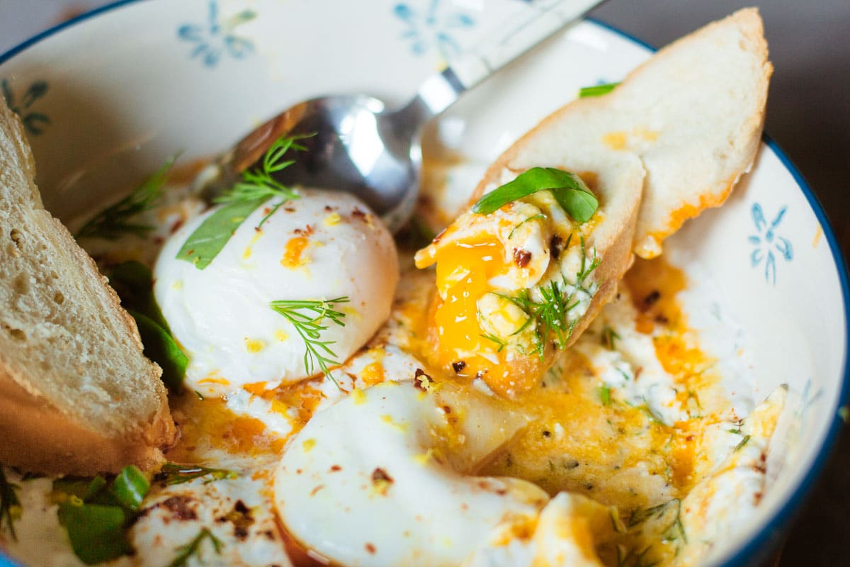 baguette slice scooping egg yolk in bowl of cilbir.