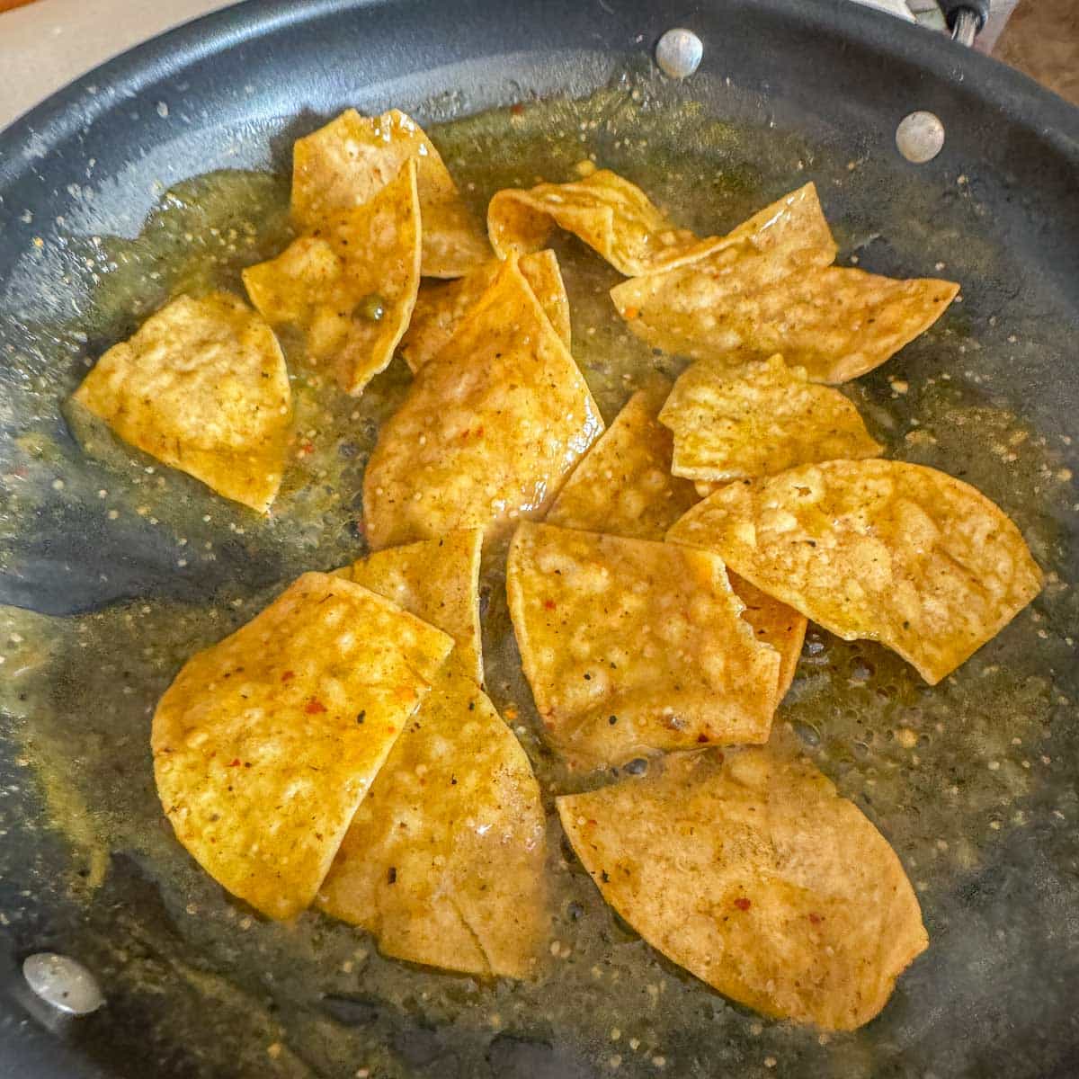 cooking tortilla chips in salsa for chilaquiles verdes.