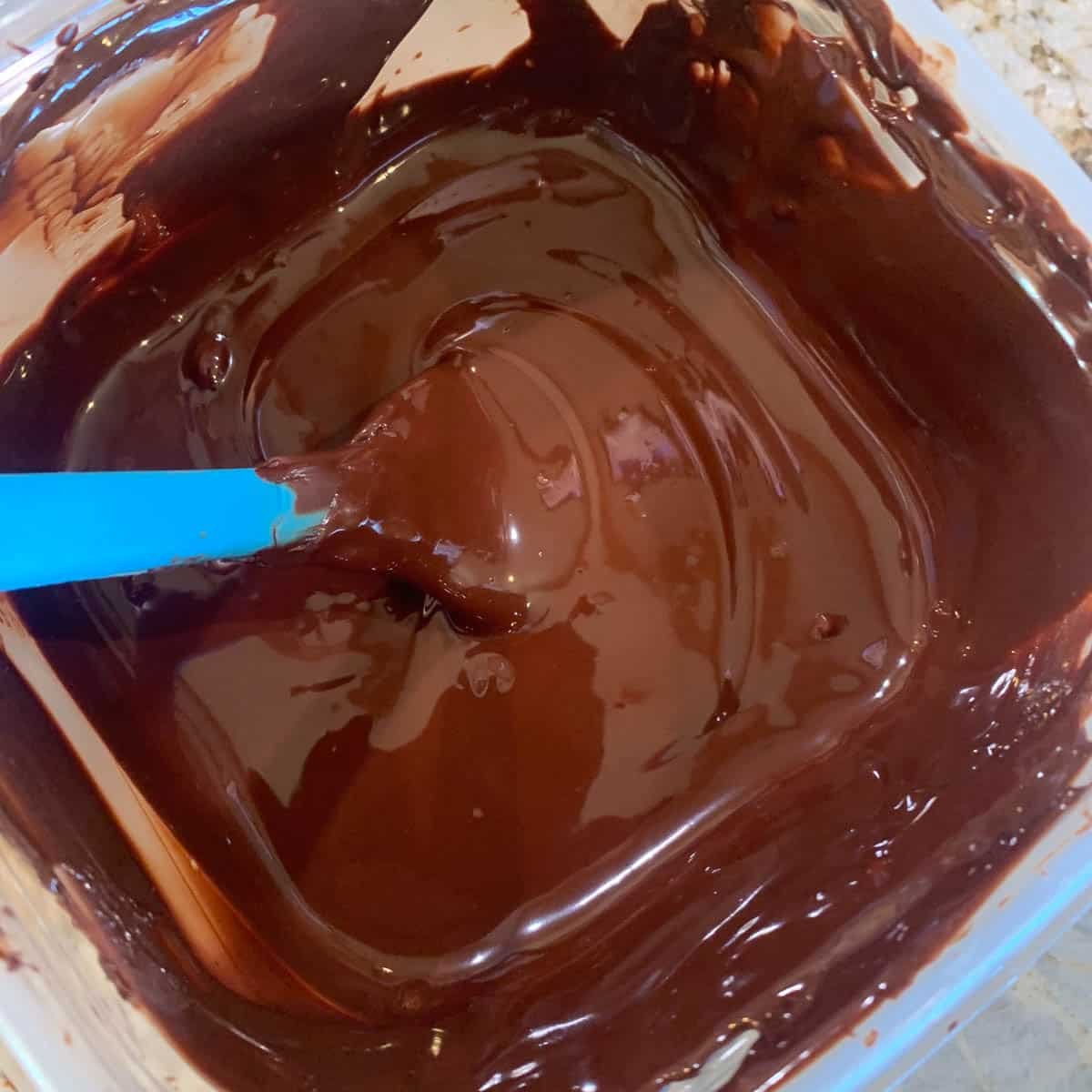 melted chocolate in a bowl with a blue spatula.