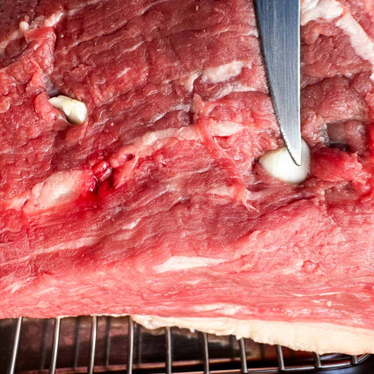raw rump roast with garlic slivers being added to slits.