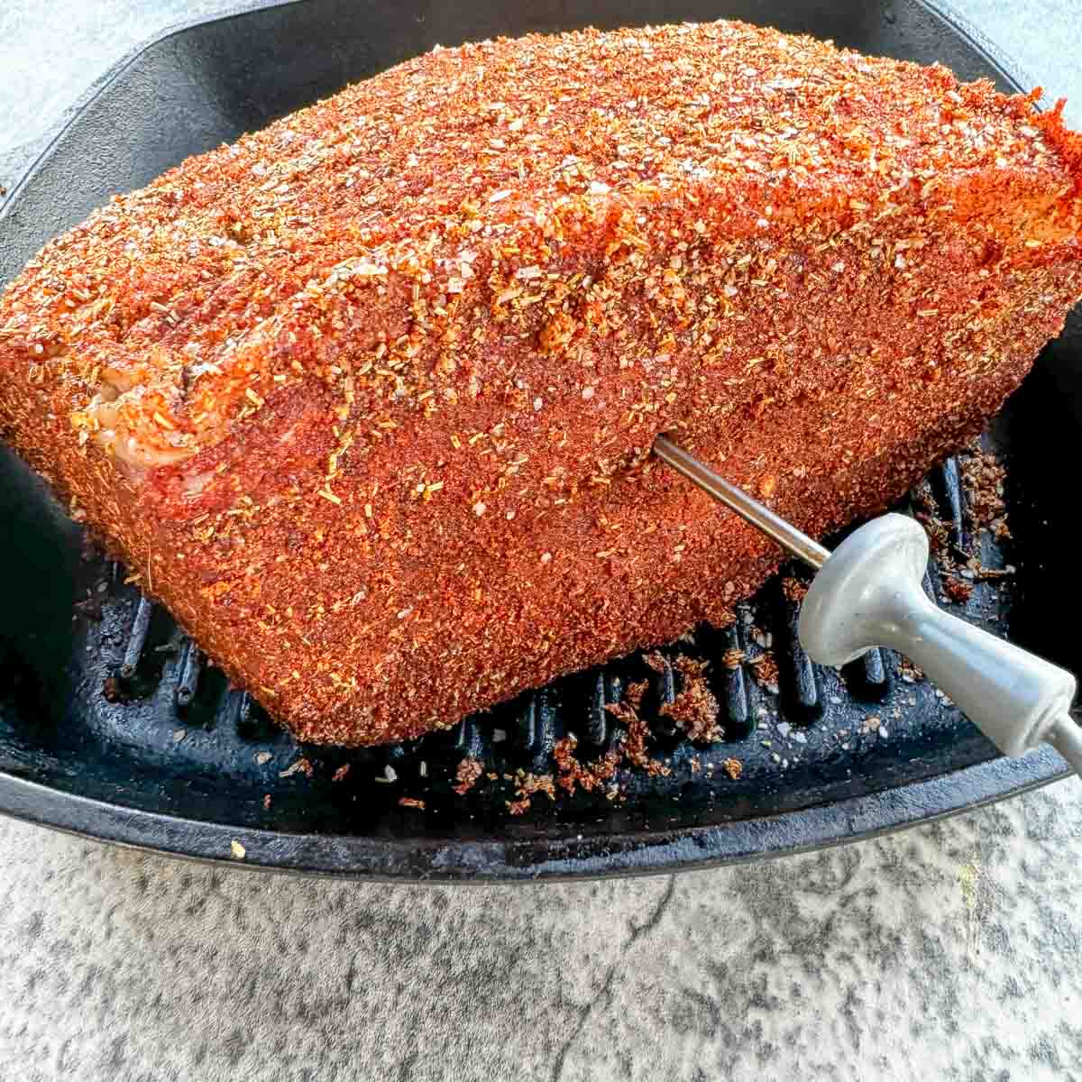 raw and seasoned bottom round roast with a meat thermometer sticking out of its side. 