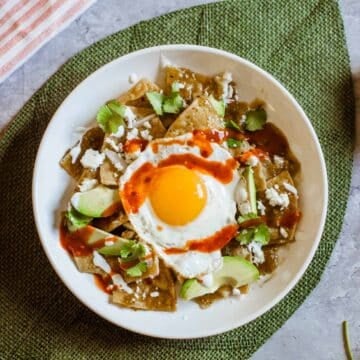 Chilaquiles verdes with an egg on top on a green mat.