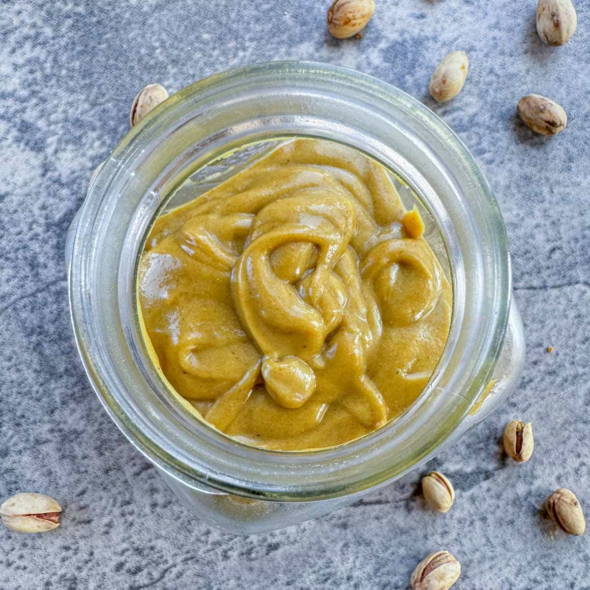 pistachio cream in a jar with pistachios around the jar.