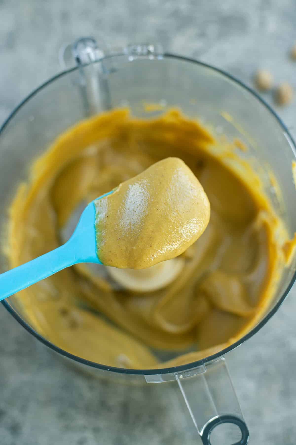 pistachio cream on a blue spatula over a food processor.
