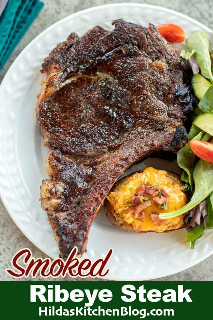 smoked ribeye steak with potato and salad on a white plate.