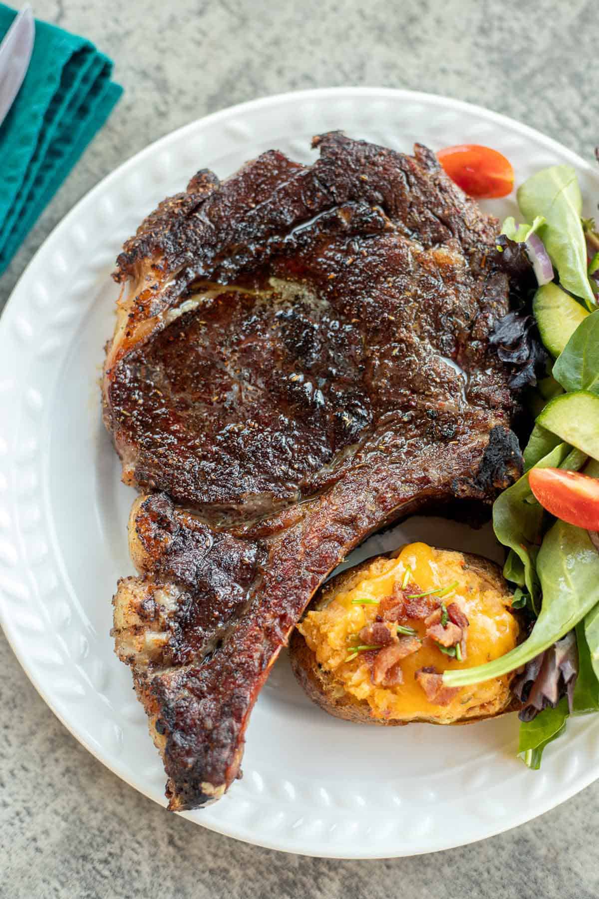 smoked ribeye steak on a plate with cheesy potato and salad.
