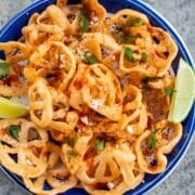 chicharrones de harina on a blue plate with lime wedges, topped with cheese and cilantro.