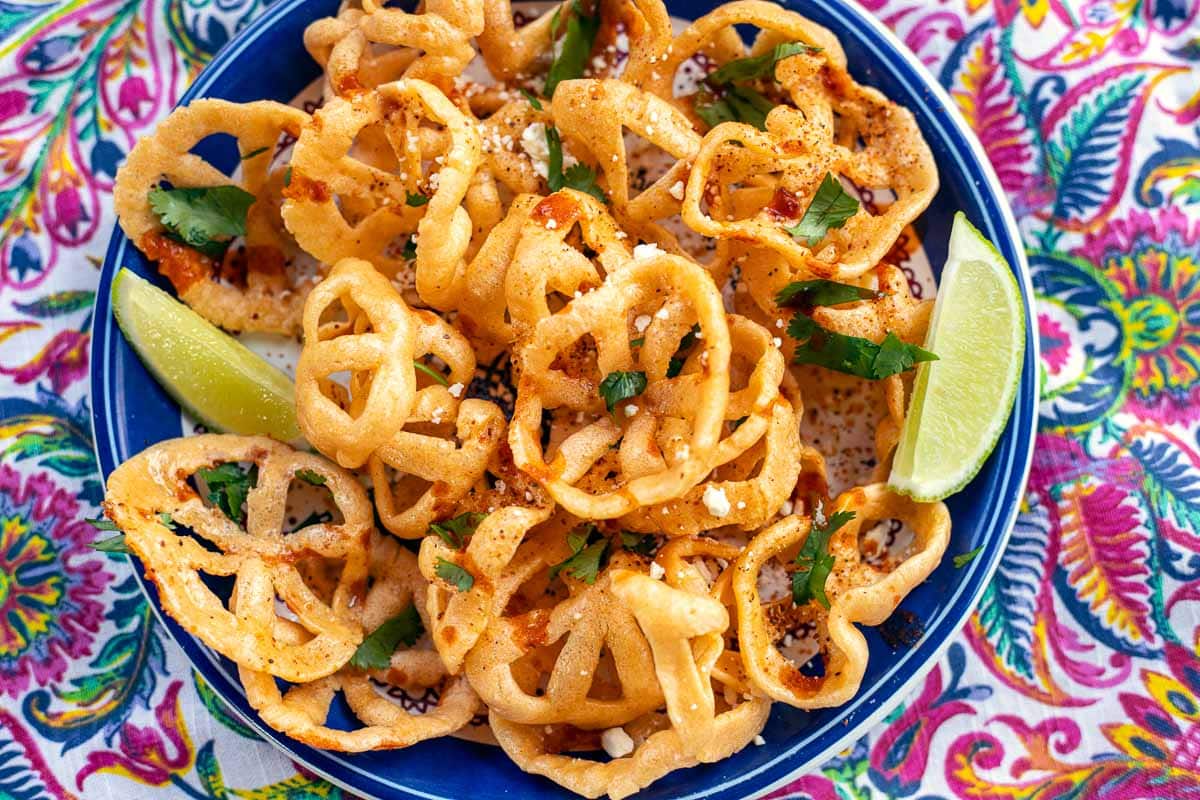 chicharrones de harina on a blue plate with 2 lime wedges with a colorful background.