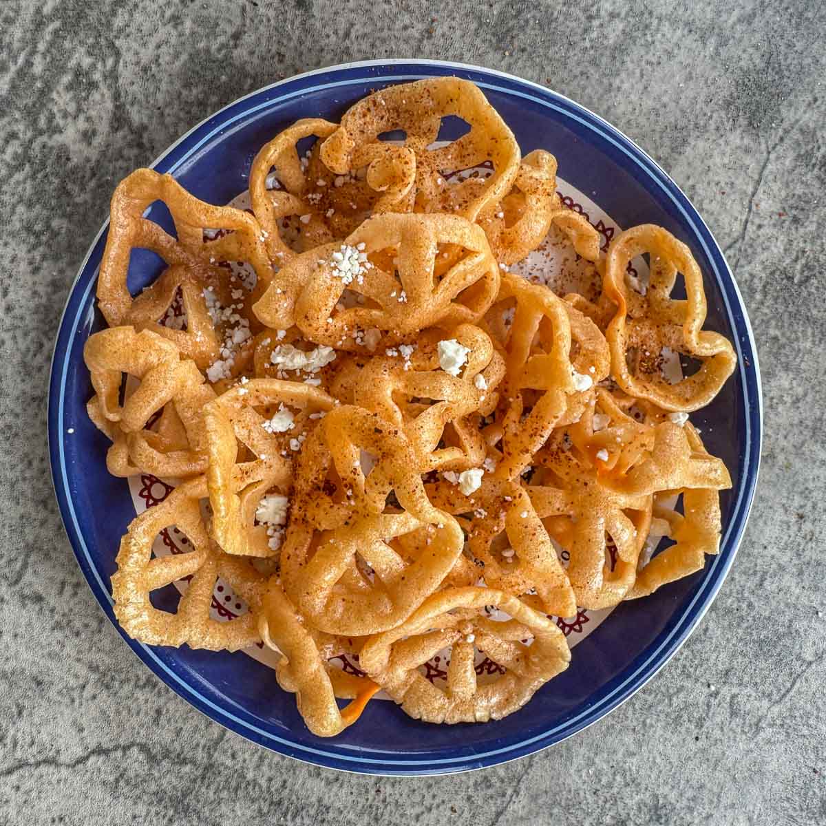 chicharrones in a blue plate seasoned and topped with cheese and cilantro.
