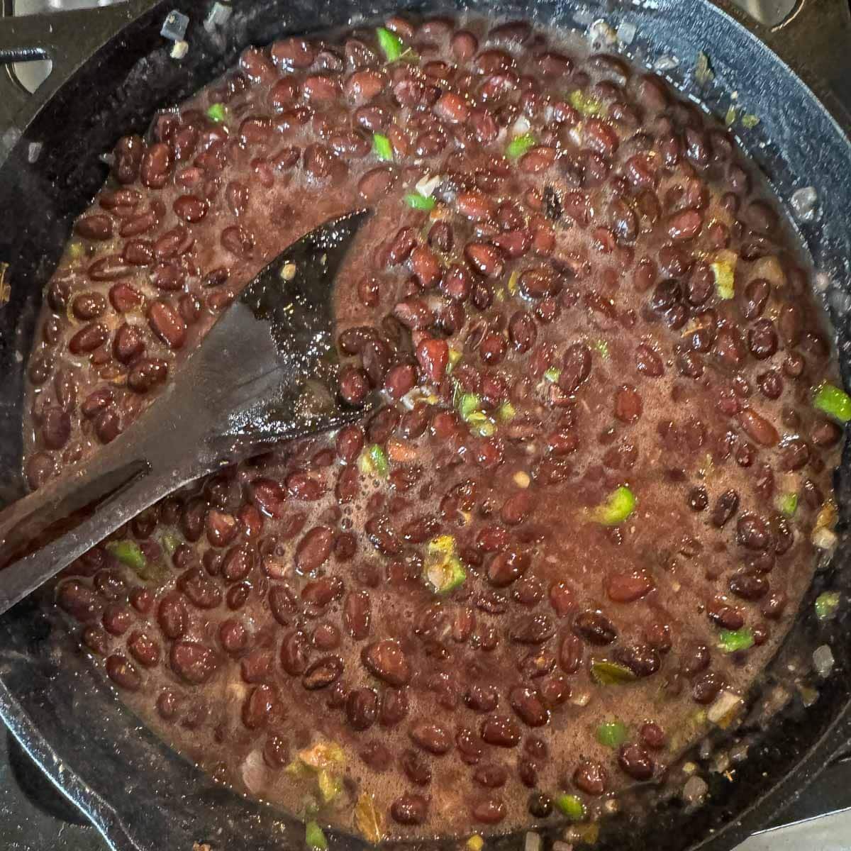 a pan of Mexican black beans with a wooden spoon. 