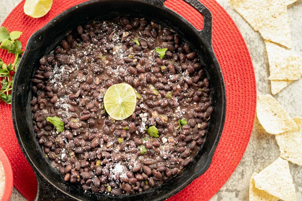 mexican black beans in a skillet with lime and tortilla chips.