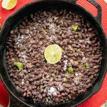 Mexican black beans in a pan with a lime slice in the middle