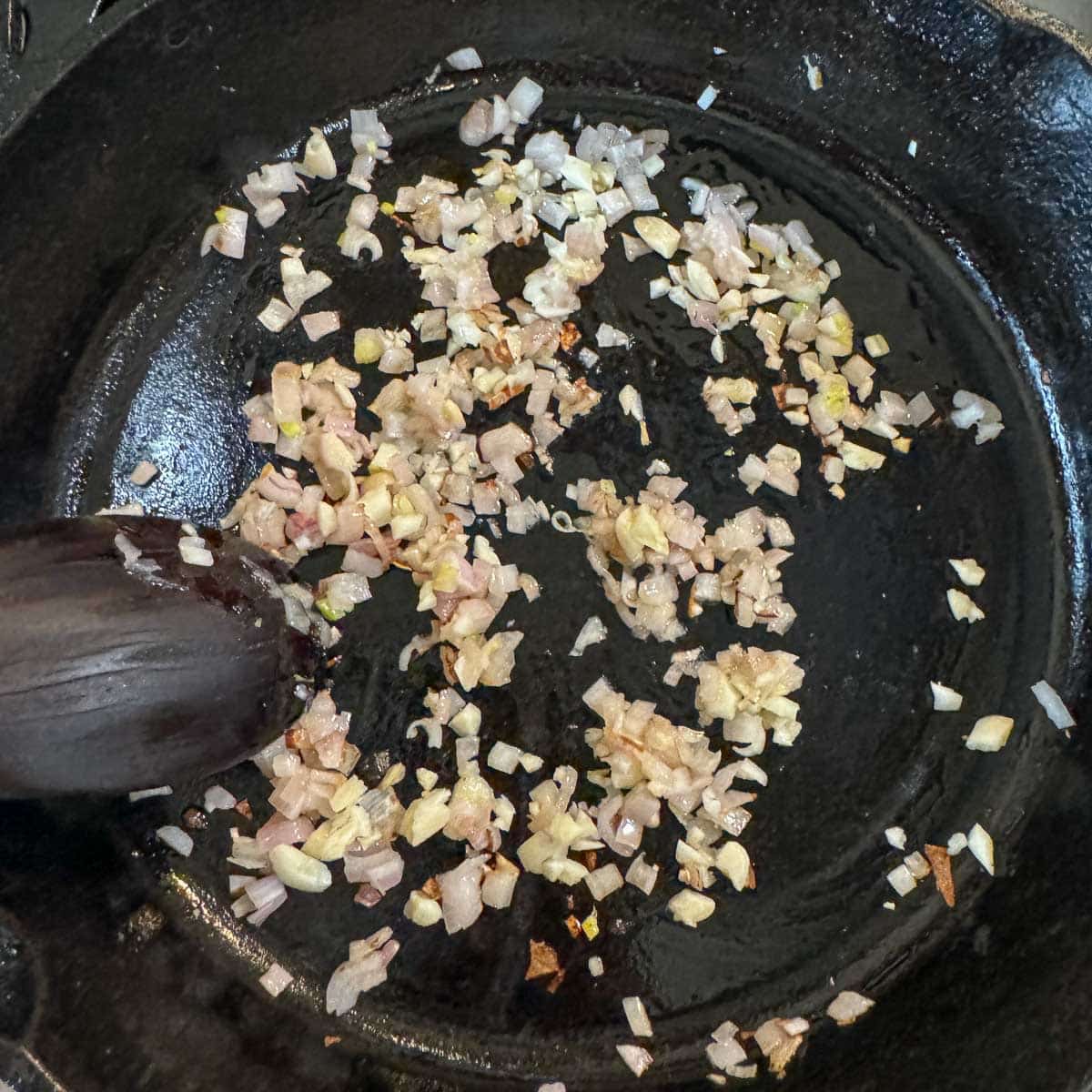 minced shallots and garlic being sauteed in a pan.