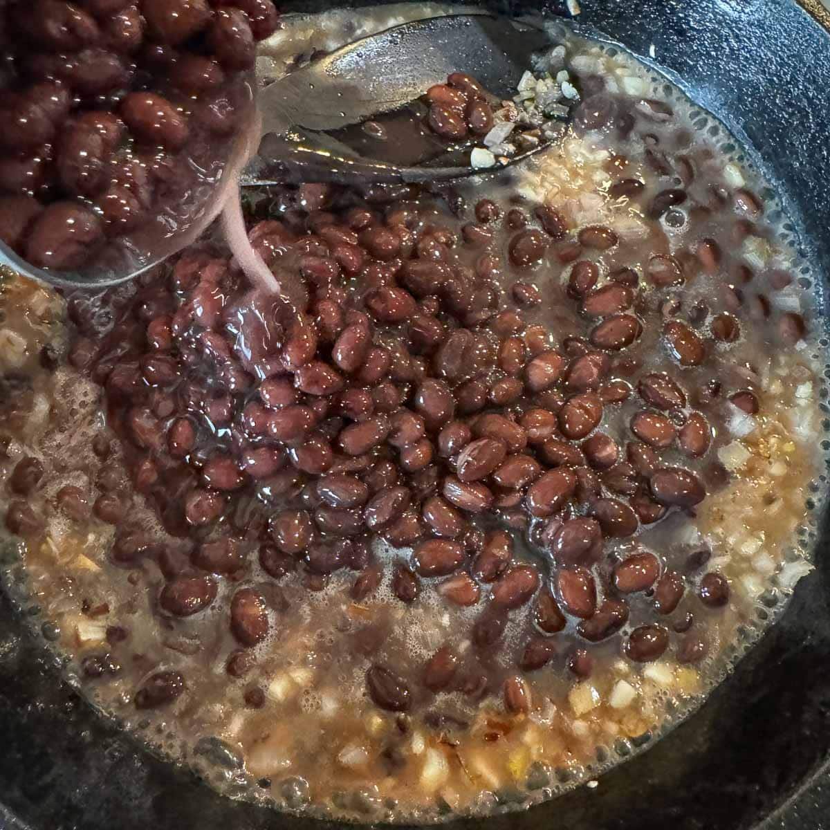 pouring canned black beans into a skillet. 