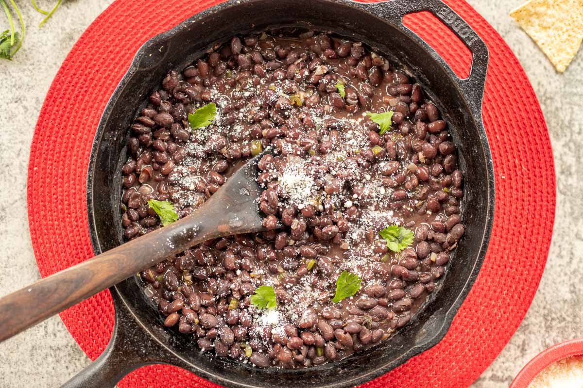 Mexican black beans in a pan over a red, round place mat.