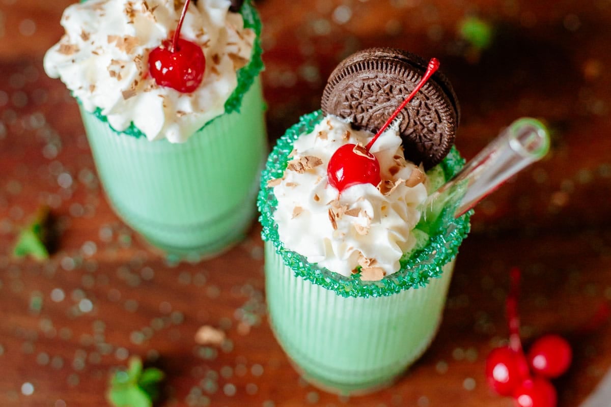 two shamrock shakes topped with whipped cream, cherries, chocolate shavings, and oreos.