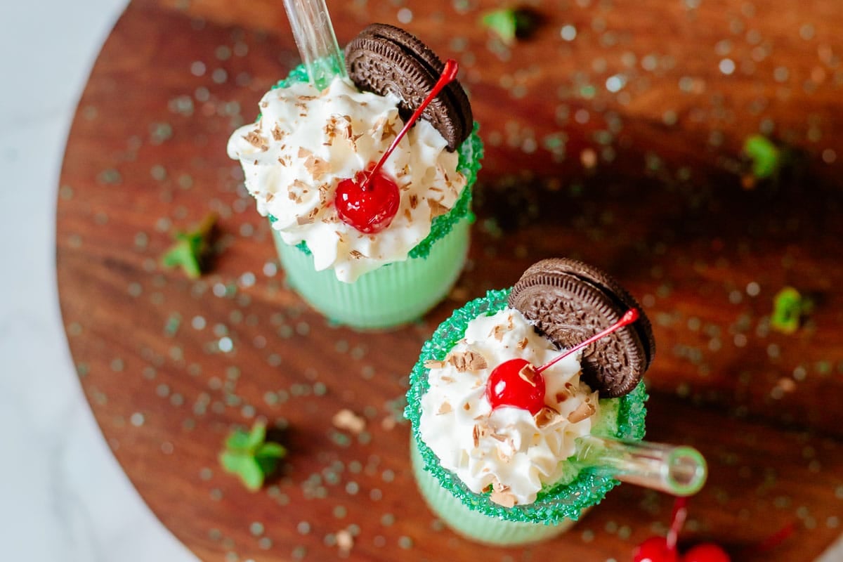 two shamrock shakes topped with whipped cream, cherries, chocolate shavings, and oreos.