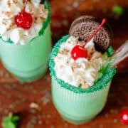 two shamrock shakes topped with whipped cream, cherries, chocolate shavings, and oreos.