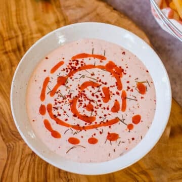 bowl of spicy ranch dip with a swirl of hot sauce on top.