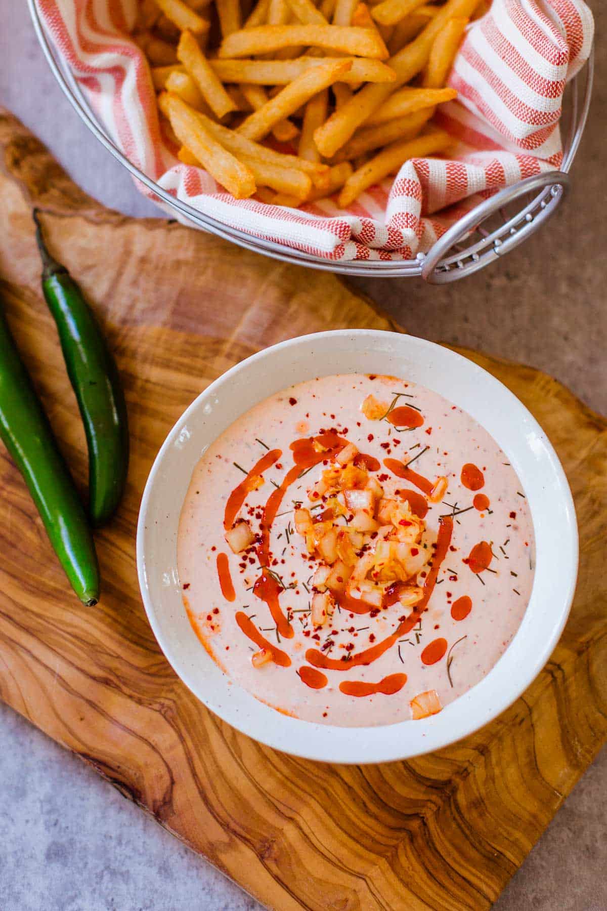 bowl of spicy ranch dip with a swirl of hot sauce and diced kimchi on top and fries and serranos on the side.