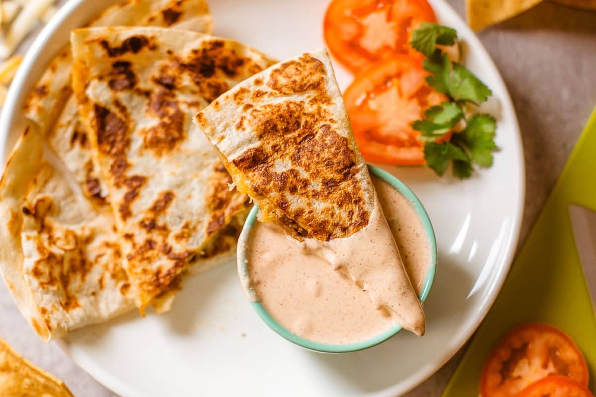 quesadilla slice dipped in sauce beside veggies and more slices.