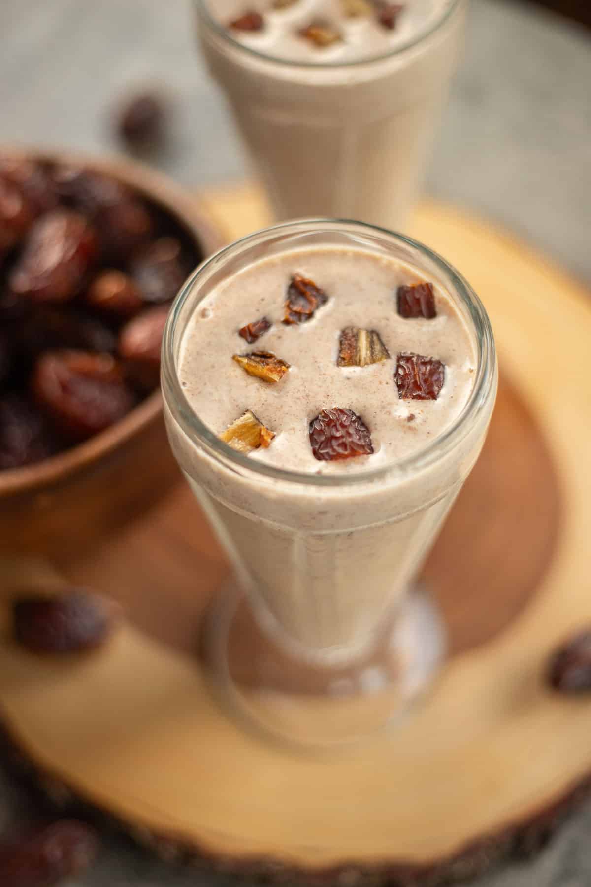 two glasses of date shake with dates in a wooden bowl next to them. 