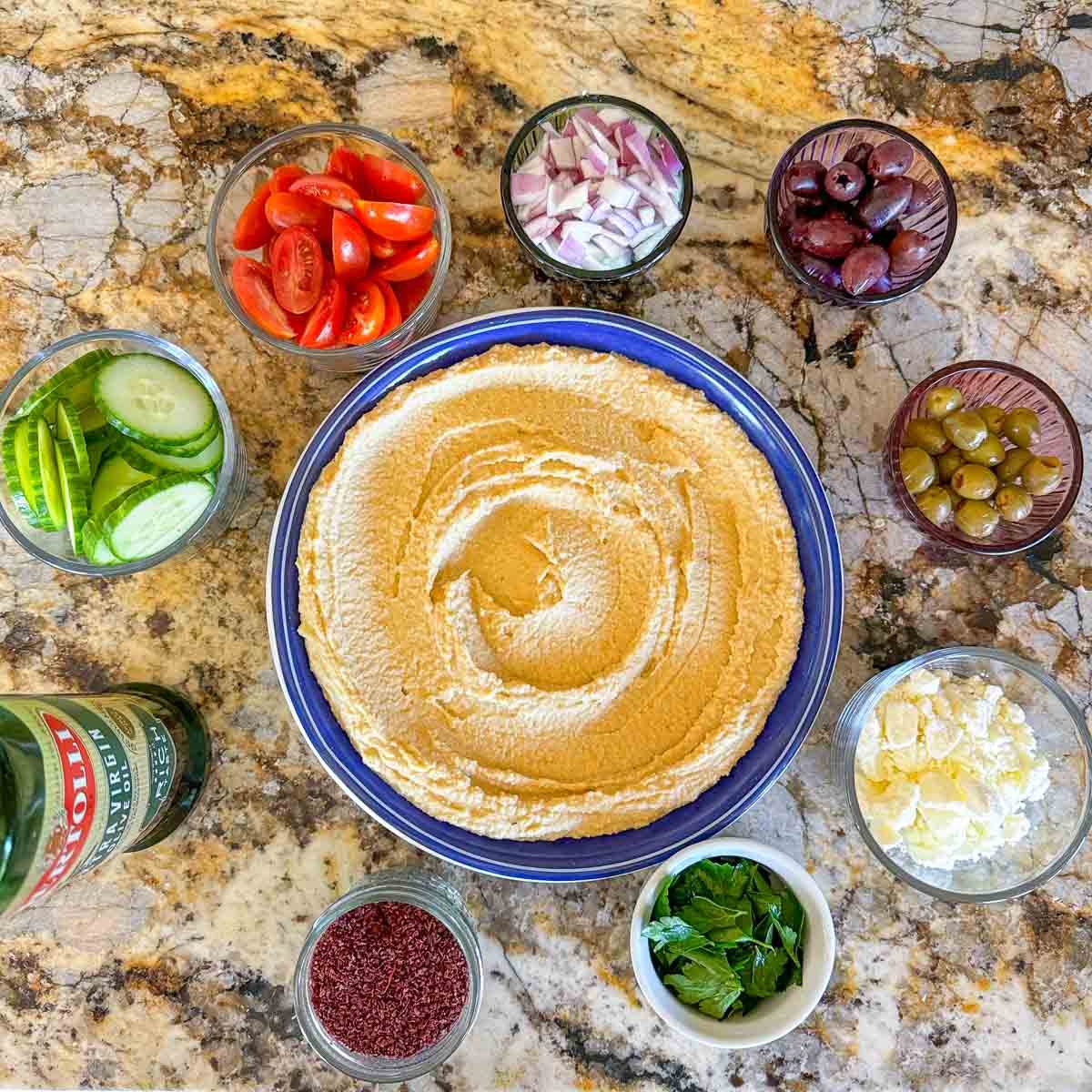 hummus in a blue plate with fresh ingredients around it.