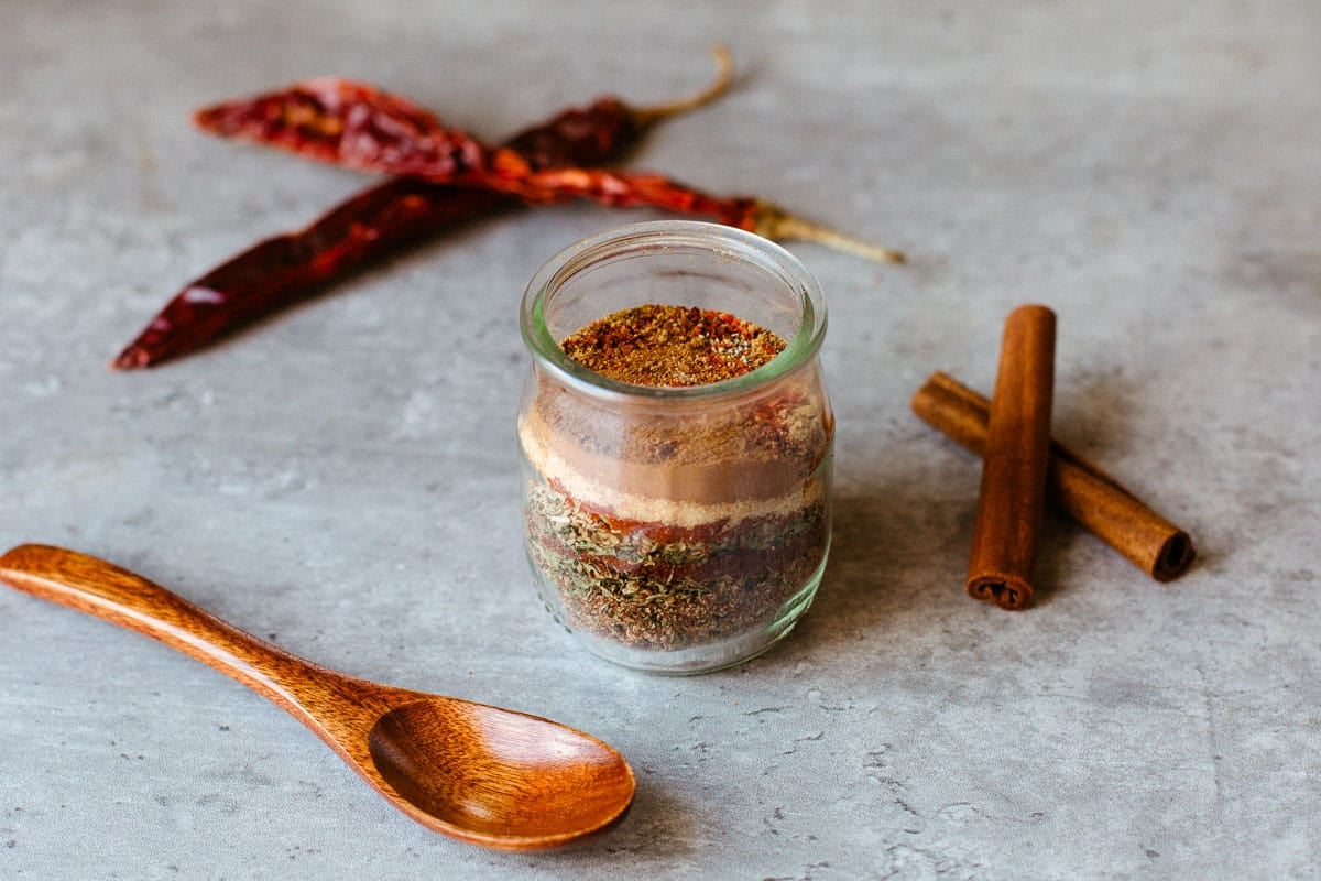 mediterranean seasoning in bottle beside spoon, cinnamon sticks, and peppers.