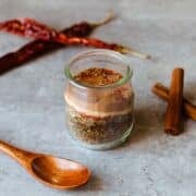 mediterranean seasoning in bottle beside spoon, cinnamon sticks, and peppers.