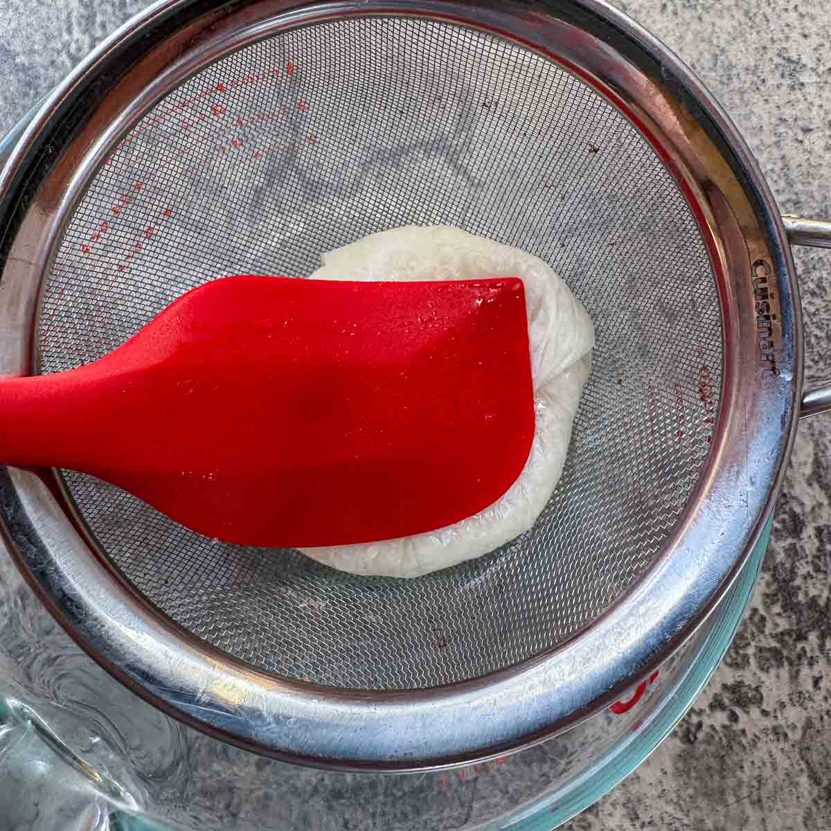 straining chopped onion through a strainer with a red spatula.