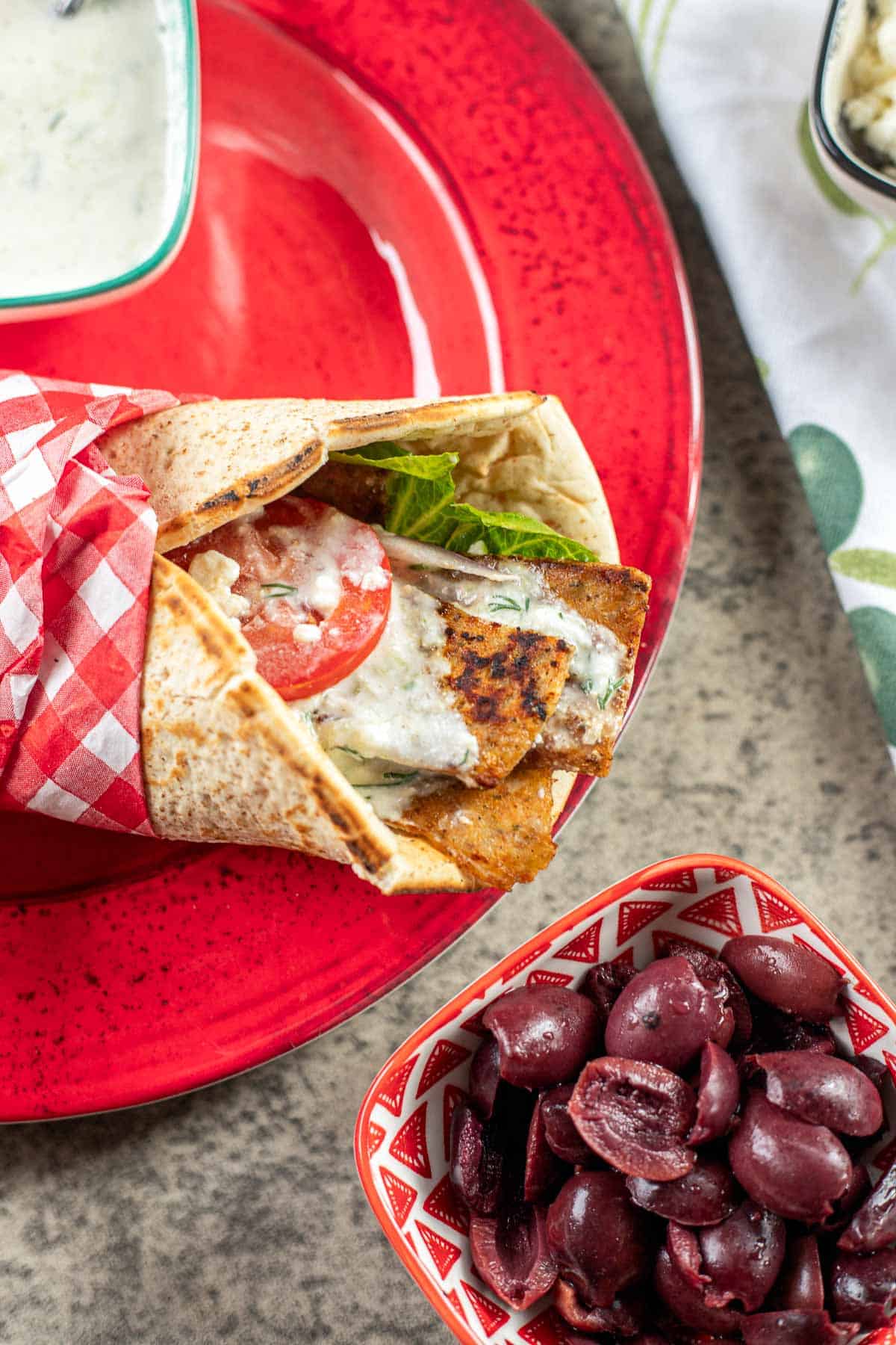 chicken gyro wrap on a red plate with olives on the side.