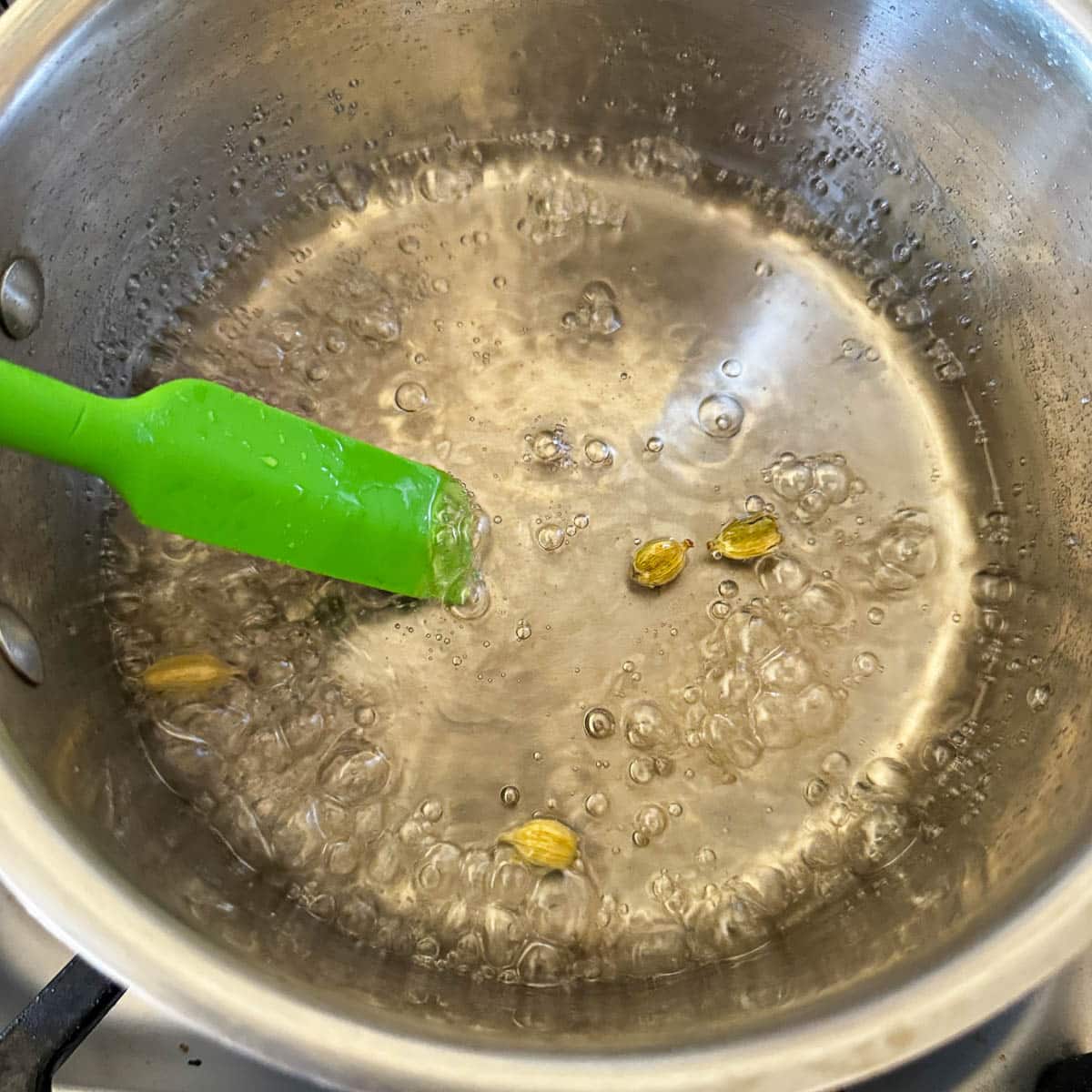 simple sugar boiling in a pot with cardamom pods.