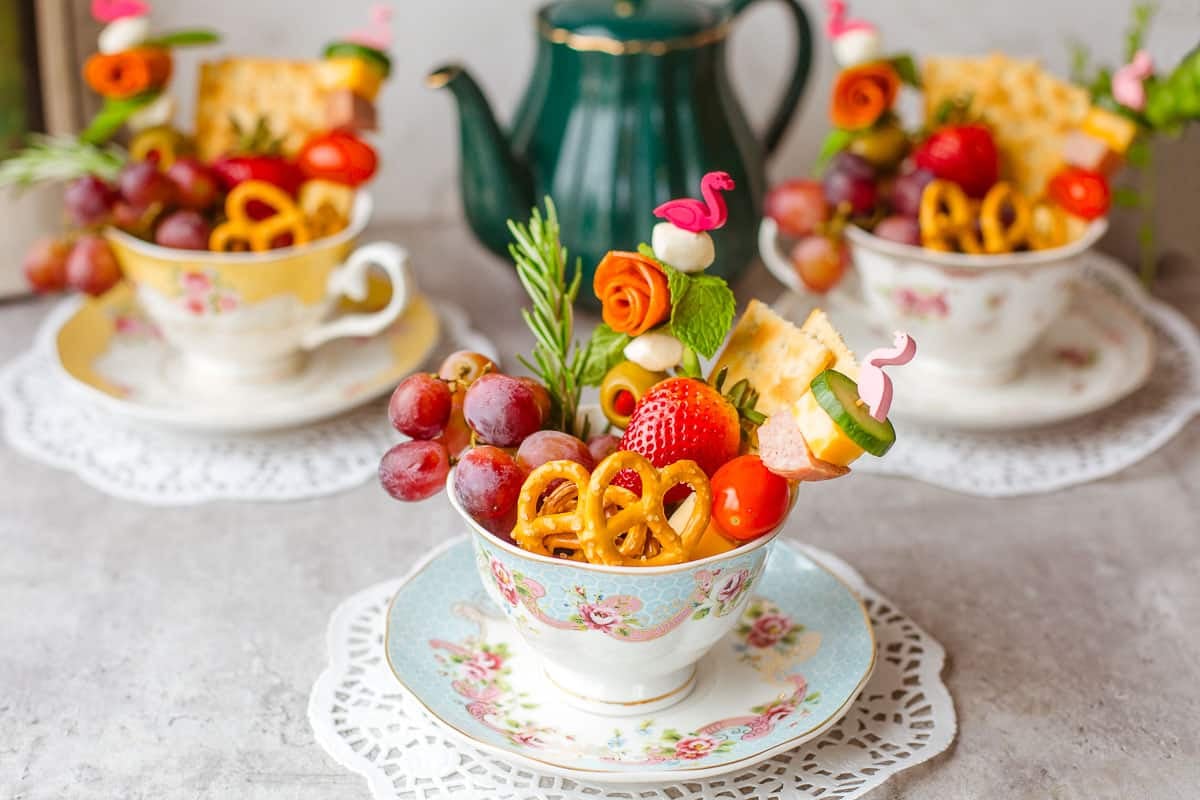 three individual charcuterie cups in teacups with teapot in background.