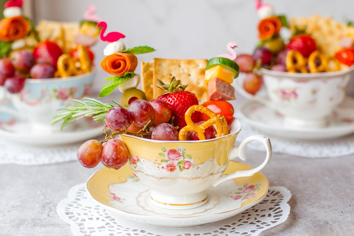 three individual charcuterie cups in teacups with teapot in background.