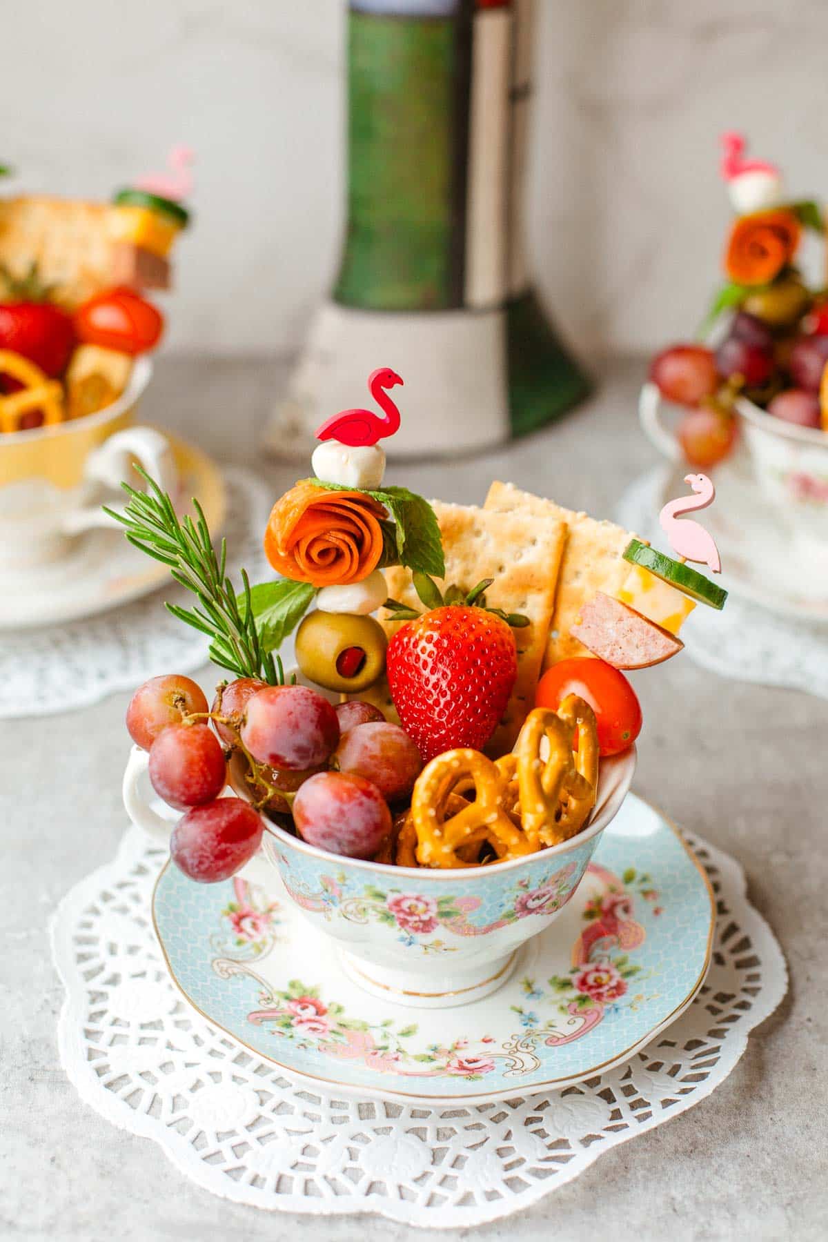 charcuterie cup full of fruits, cheese, meats. pretzels, etc. and more cups in background.