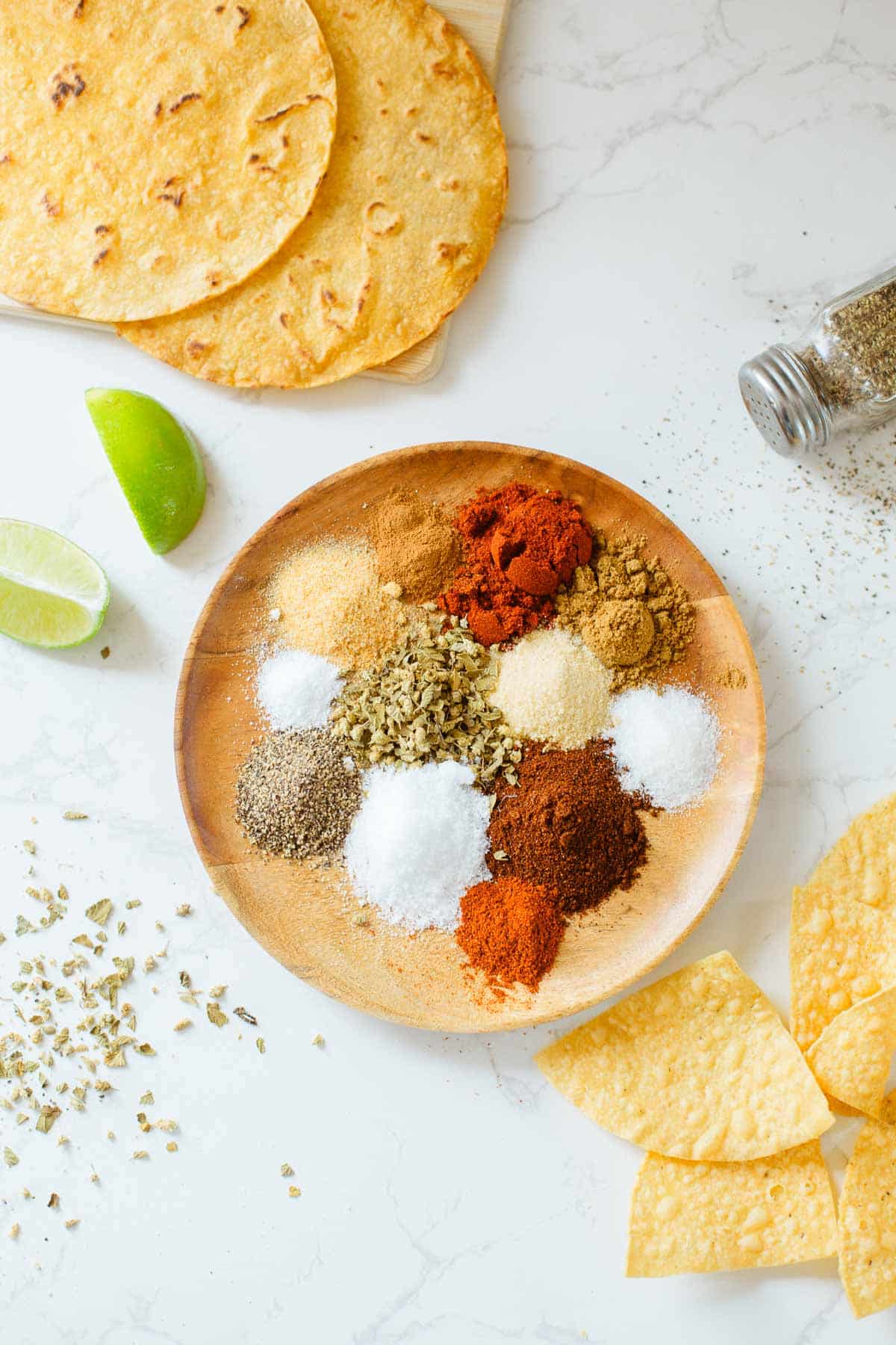 homemade taco seasoning recipe ingredients on plate before mixing, surrounded by tortillas, lime, spices.