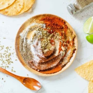 chicken taco seasoning on a plate after being partially mixed, surrounded by tortillas, spoon, lime, spices.