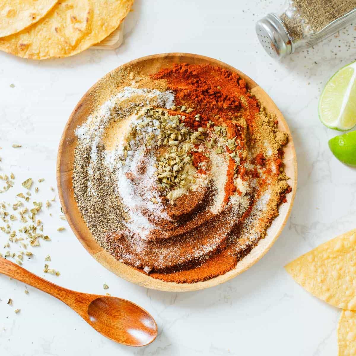 chicken taco seasoning on a plate after being partially mixed, surrounded by tortillas, spoon, lime, spices.